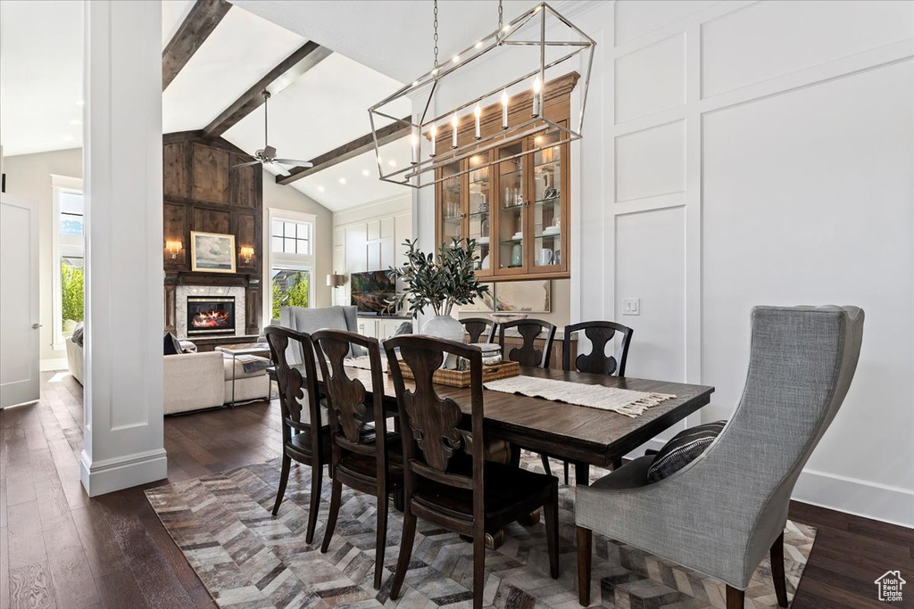 Dining space with ceiling fan, a large fireplace, beamed ceiling, dark hardwood / wood-style flooring, and high vaulted ceiling