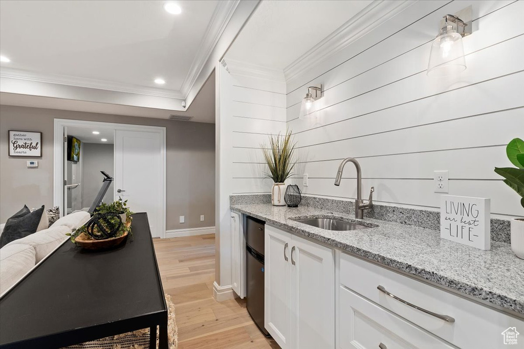 Kitchen with light stone countertops, dishwasher, light wood-type flooring, sink, and white cabinetry