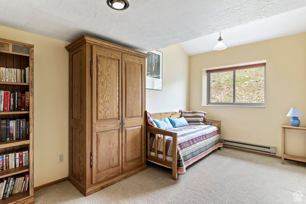 Carpeted bedroom featuring a baseboard heating unit and a textured ceiling