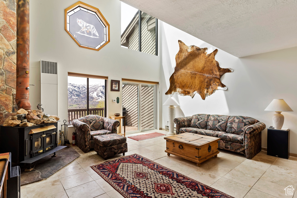 Living room featuring a high ceiling, tile floors, a wood stove, and a textured ceiling