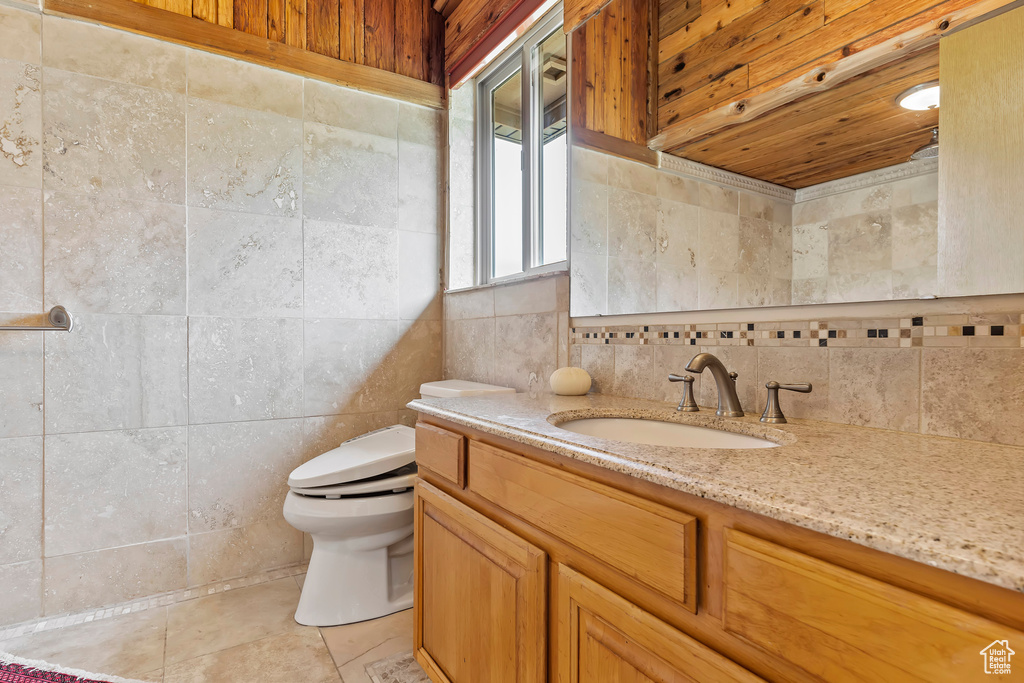 Bathroom featuring tile walls, tile flooring, toilet, and vanity with extensive cabinet space