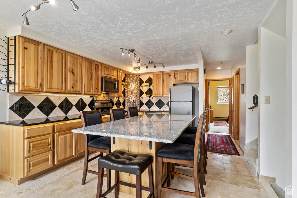 Kitchen featuring a baseboard radiator, a kitchen island, appliances with stainless steel finishes, track lighting, and tasteful backsplash