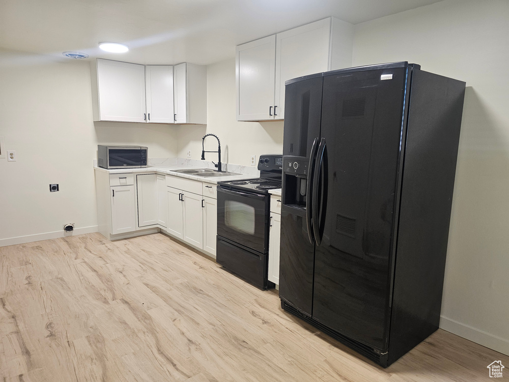 Kitchen featuring black appliances, white cabinets, sink, and light hardwood / wood-style flooring