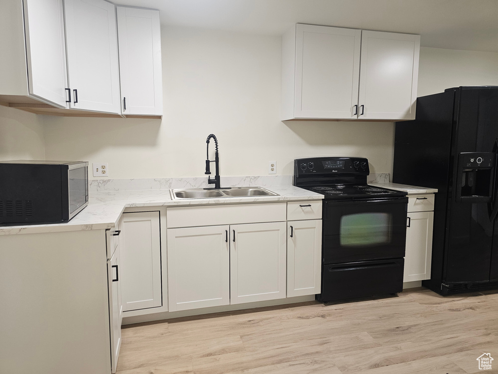 Kitchen featuring black appliances, sink, white cabinetry, and light hardwood / wood-style flooring