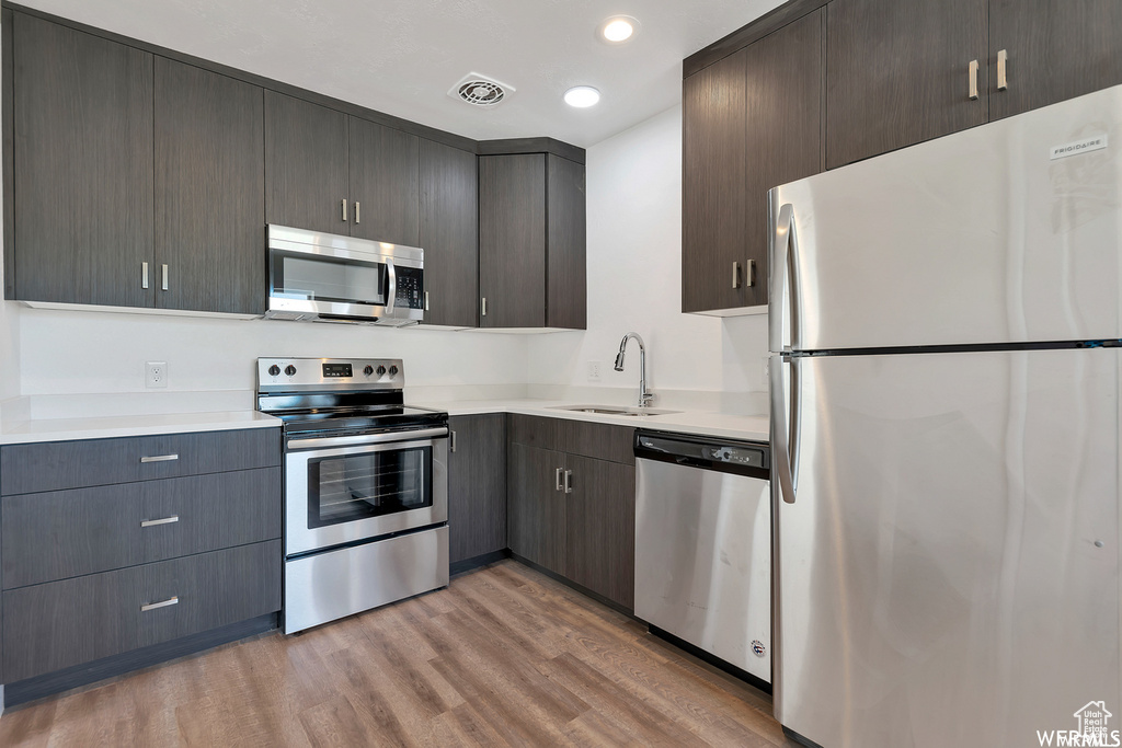 Kitchen featuring dark brown cabinets, stainless steel appliances, hardwood / wood-style floors, and sink