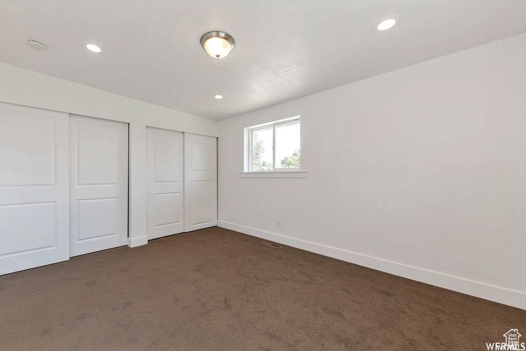 Unfurnished bedroom featuring dark colored carpet and multiple closets