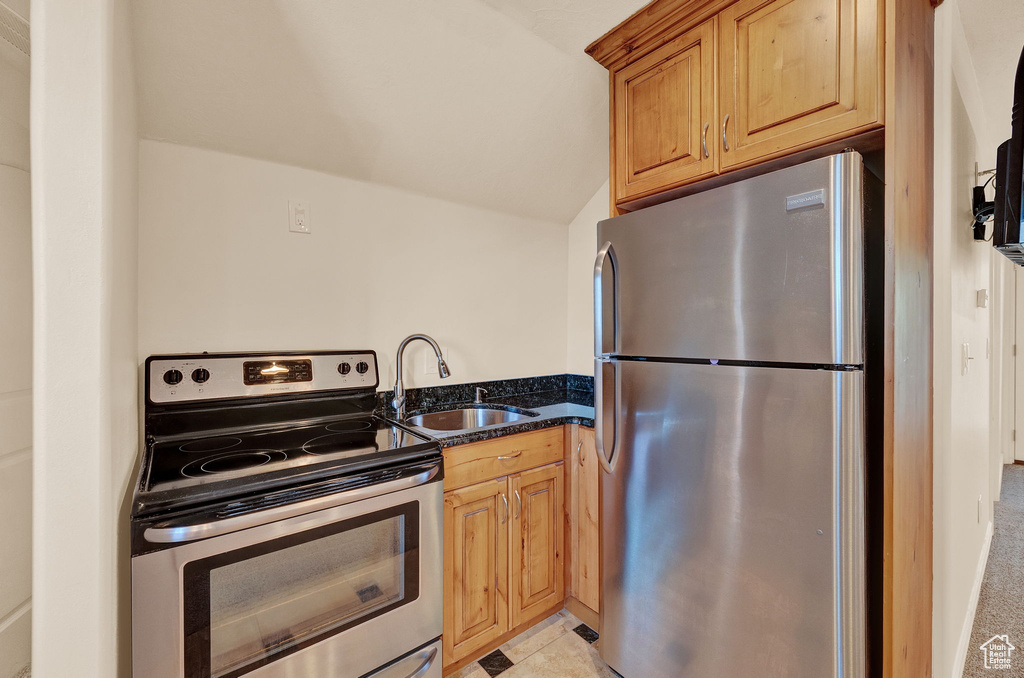 Kitchen featuring appliances with stainless steel finishes, sink, dark stone countertops, and light tile floors