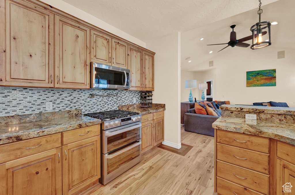 Kitchen with ceiling fan, light hardwood / wood-style floors, vaulted ceiling, backsplash, and appliances with stainless steel finishes