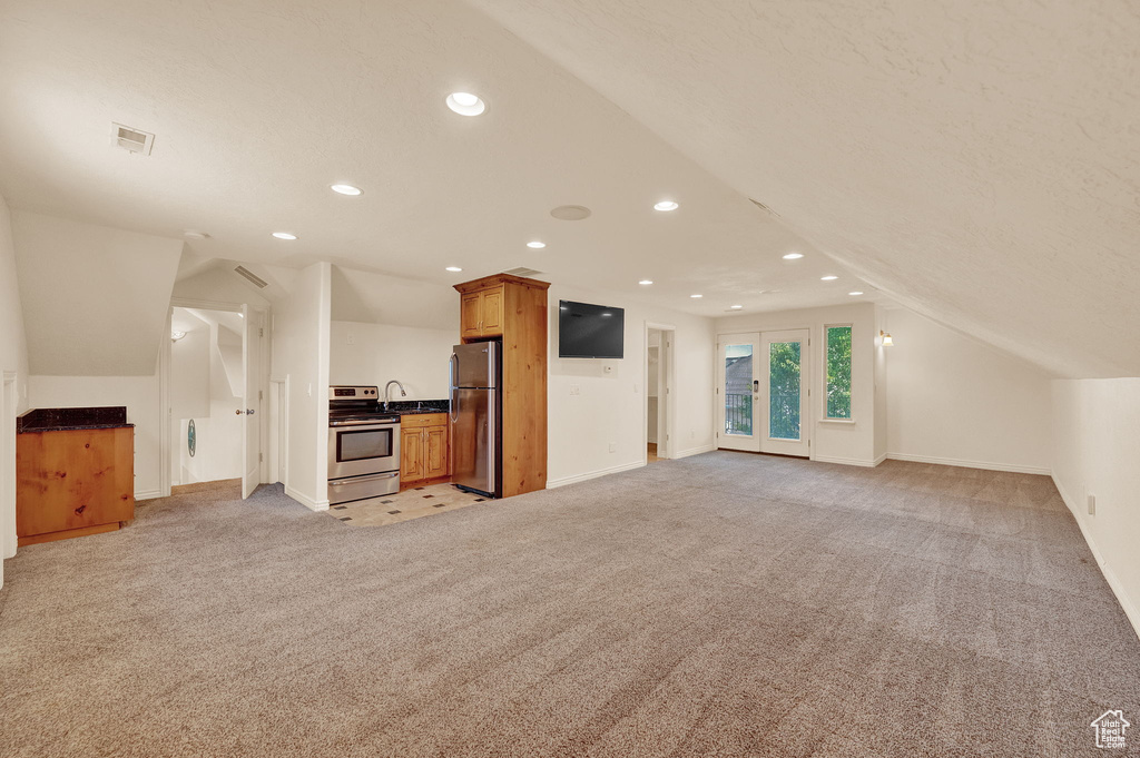 Unfurnished living room featuring vaulted ceiling, light carpet, sink, and french doors