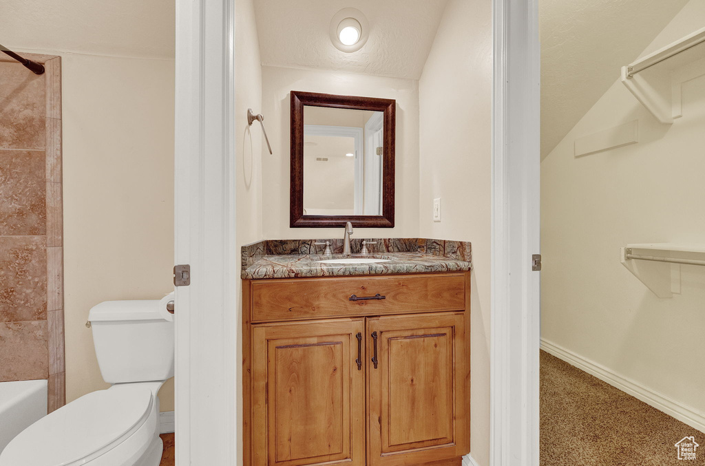 Full bathroom with vaulted ceiling, tiled shower / bath combo, vanity, and toilet