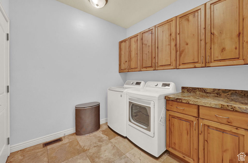 Clothes washing area with cabinets, light tile flooring, and independent washer and dryer