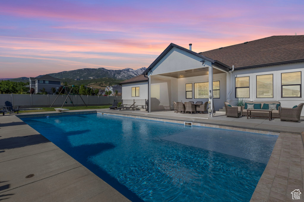 Pool at dusk with a diving board, a mountain view, an outdoor living space, and a patio area