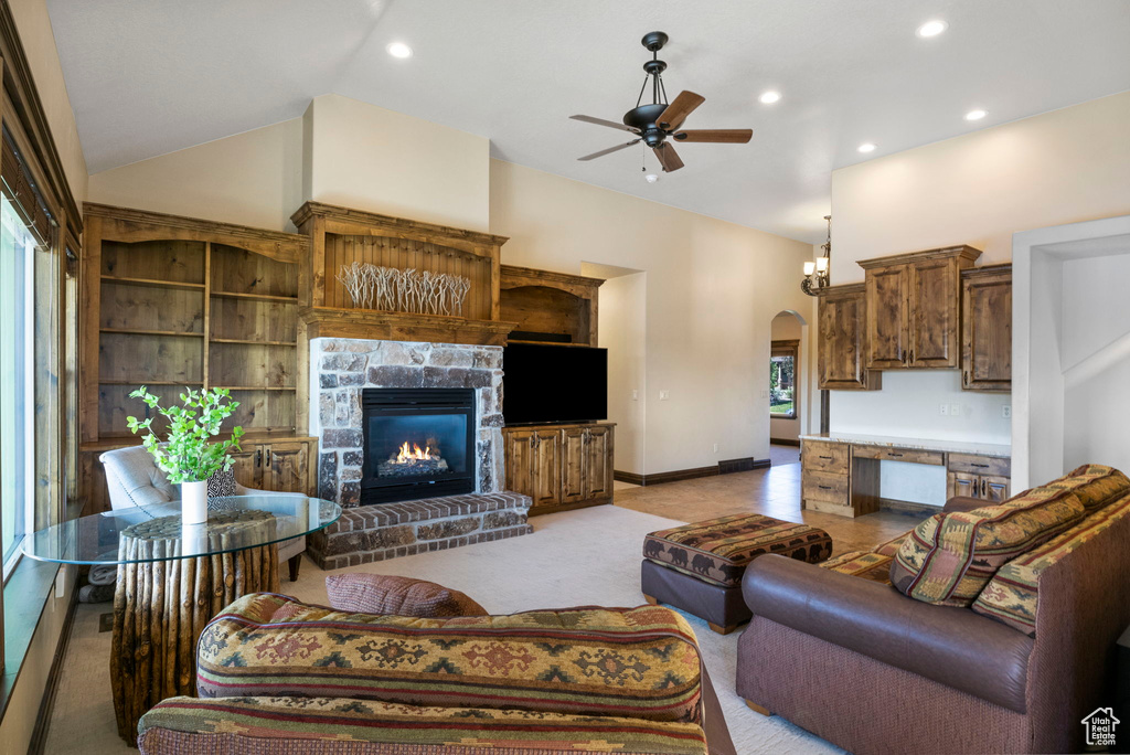 Carpeted living room with a stone fireplace, ceiling fan, a wealth of natural light, and high vaulted ceiling