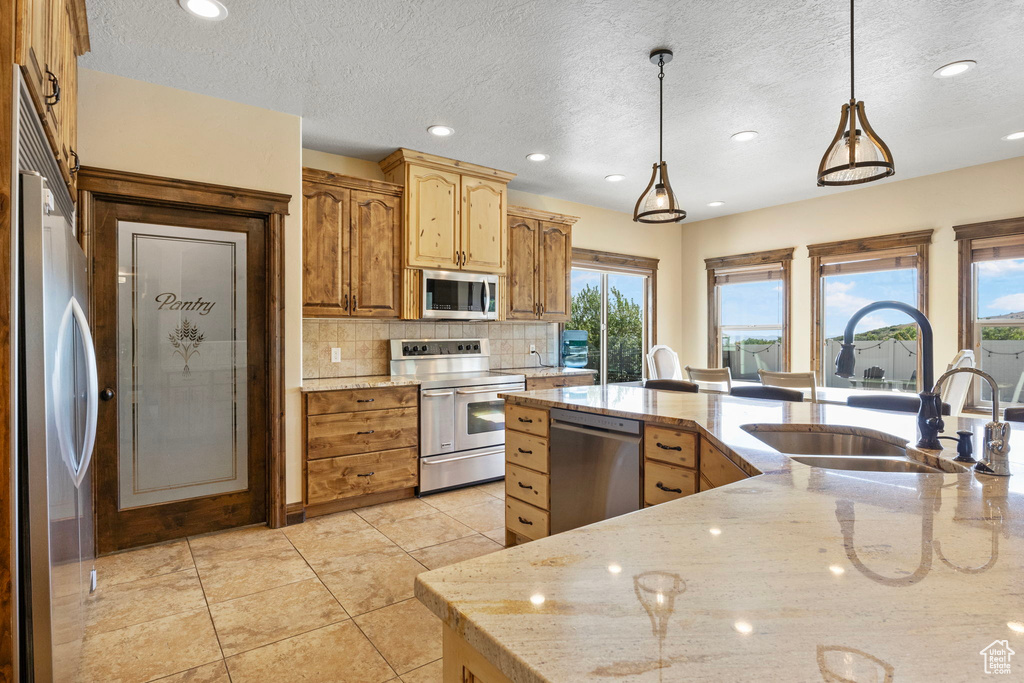 Kitchen with light stone countertops, tasteful backsplash, stainless steel appliances, decorative light fixtures, and sink