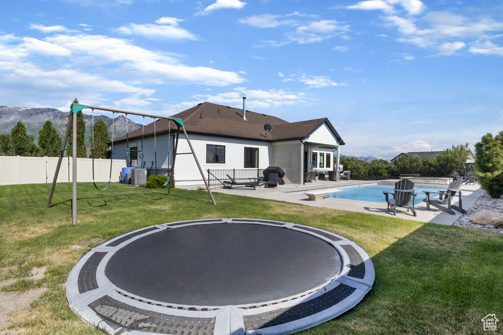 Rear view of property featuring a patio area, a yard, central AC, and a fenced in pool