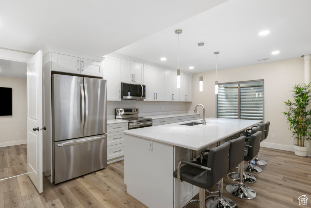 Kitchen featuring light hardwood / wood-style floors, white cabinetry, a center island with sink, stainless steel appliances, and sink