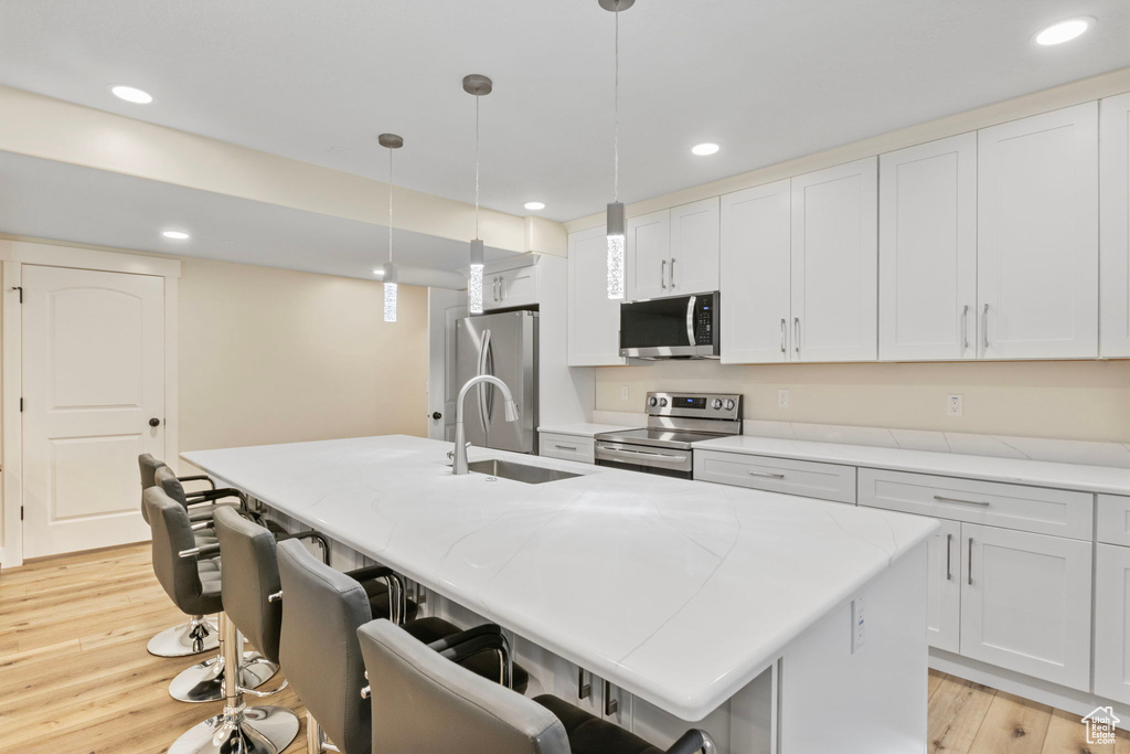 Kitchen with a center island with sink, light hardwood / wood-style flooring, decorative light fixtures, and appliances with stainless steel finishes