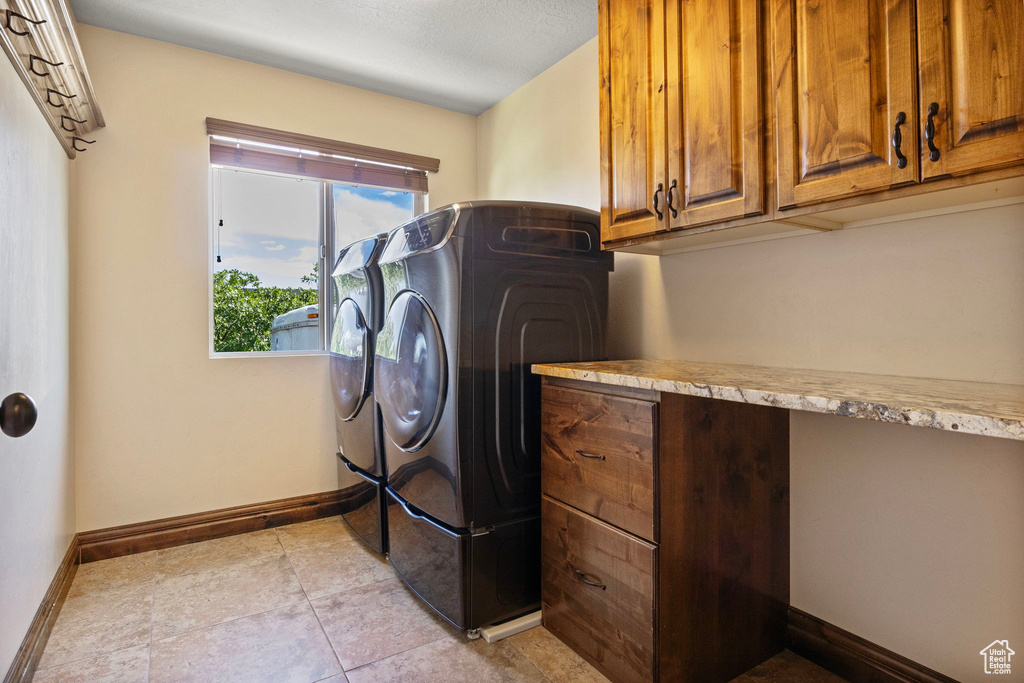 Laundry room with washing machine and dryer, light tile flooring, and cabinets