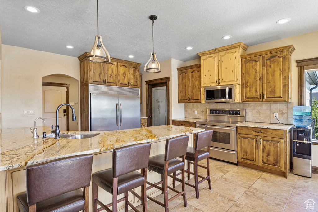 Kitchen with appliances with stainless steel finishes, decorative light fixtures, backsplash, sink, and light tile floors