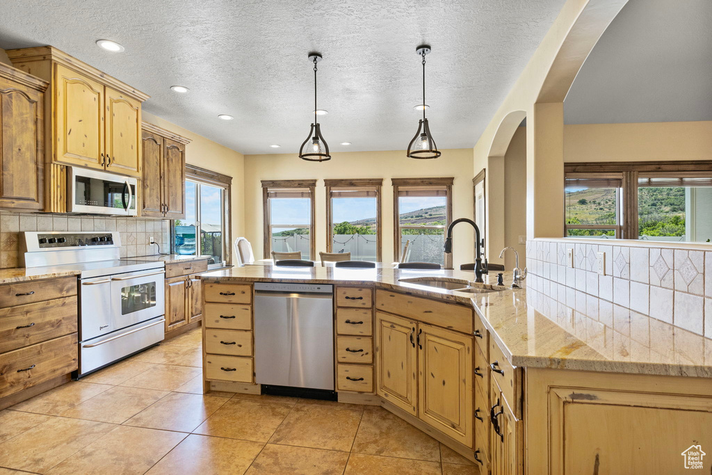 Kitchen with tasteful backsplash, light tile floors, hanging light fixtures, sink, and appliances with stainless steel finishes