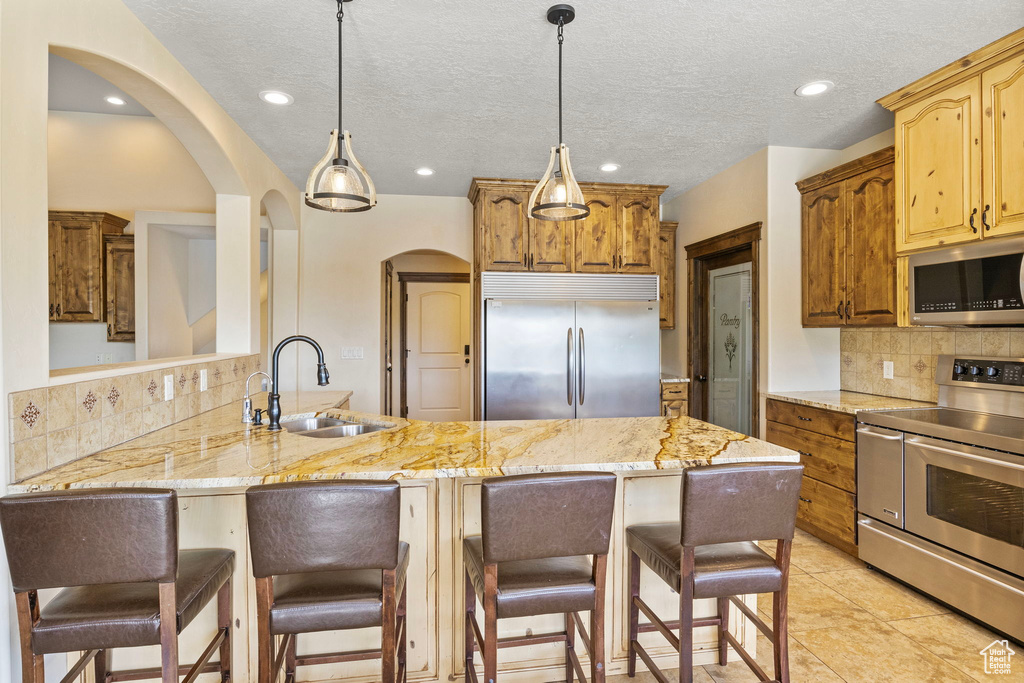 Kitchen with backsplash, appliances with stainless steel finishes, sink, light tile floors, and pendant lighting