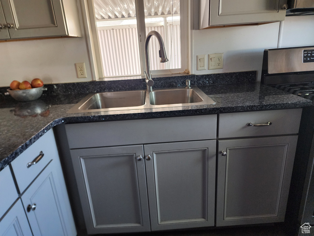 Kitchen featuring sink, dark stone counters, stove, and gray cabinets