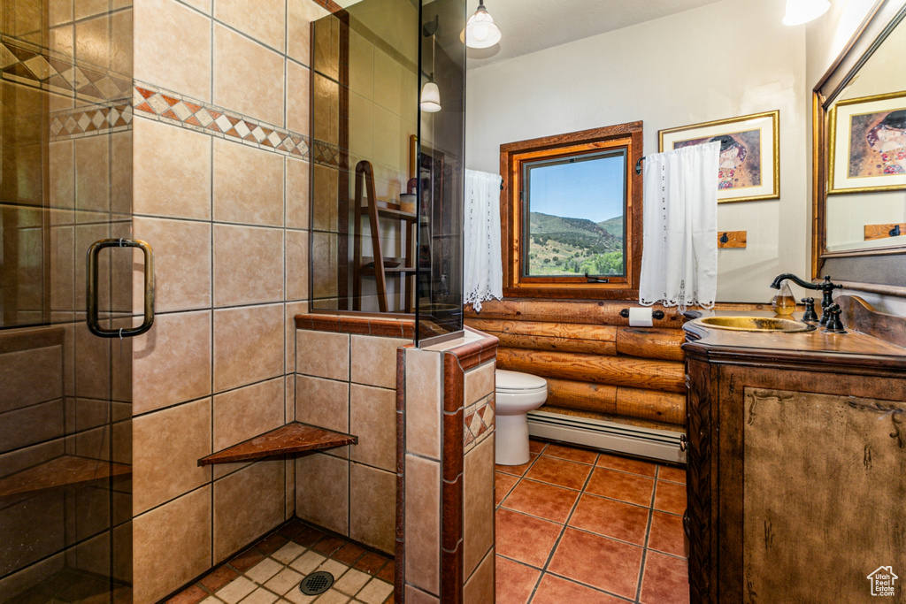 Bathroom with a baseboard heating unit, a shower with shower door, tile floors, large vanity, and toilet