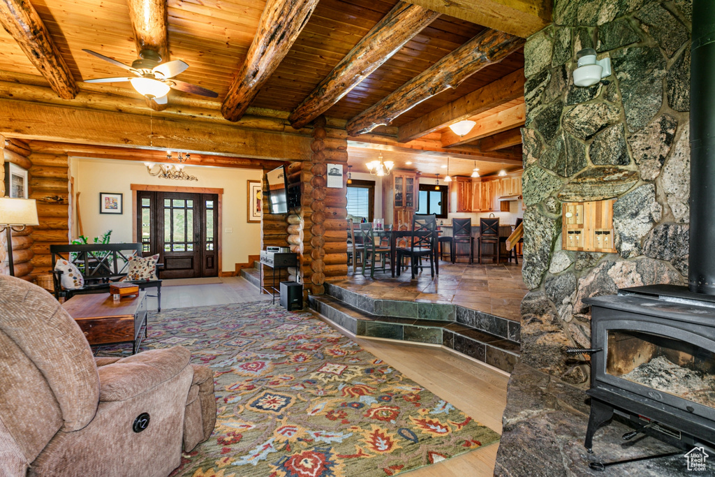 Living room featuring wooden ceiling, beam ceiling, a wood stove, rustic walls, and ceiling fan