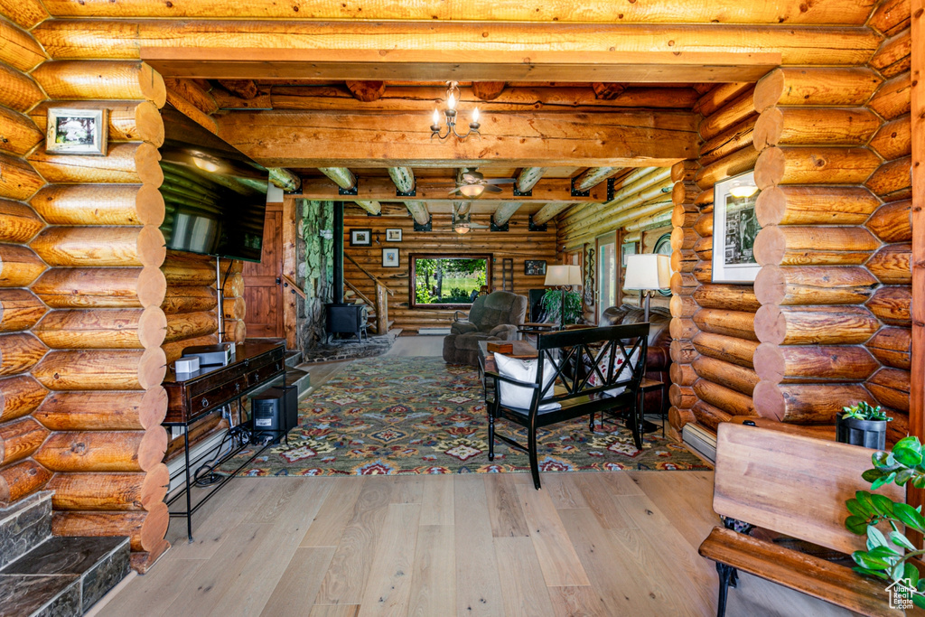 Unfurnished living room with beam ceiling, a wood stove, wood-type flooring, and log walls