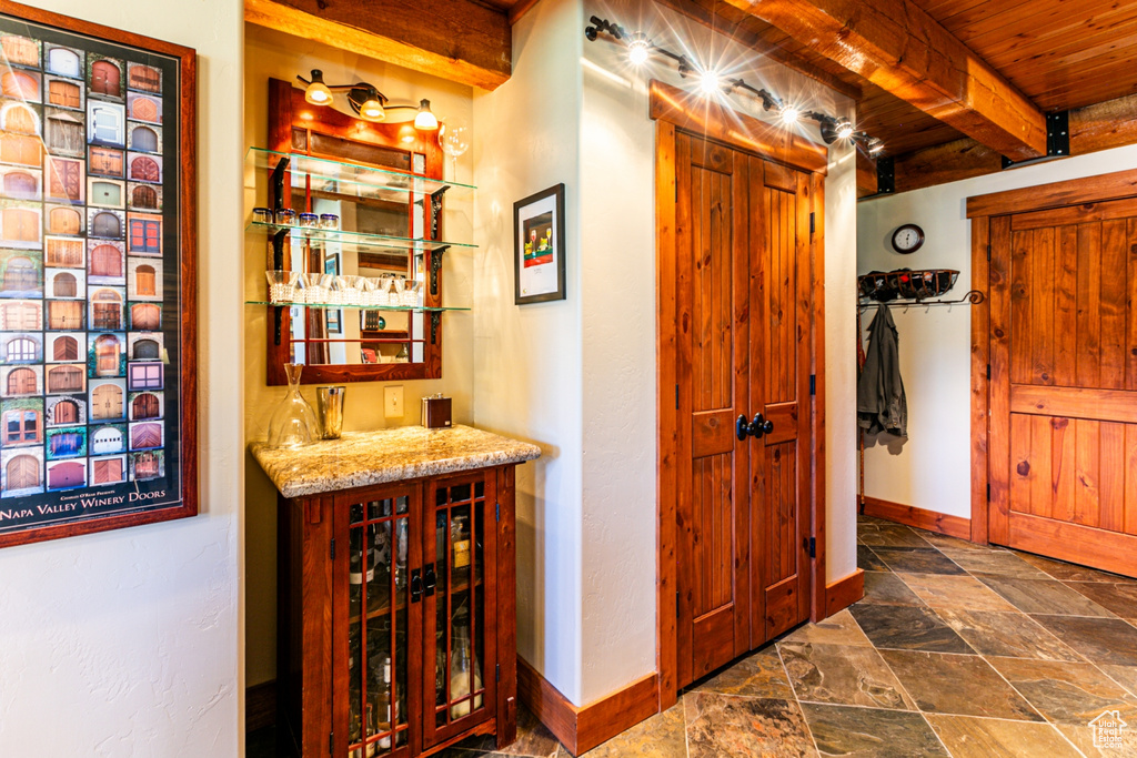 Bar with beam ceiling, light stone countertops, wood ceiling, and dark tile flooring