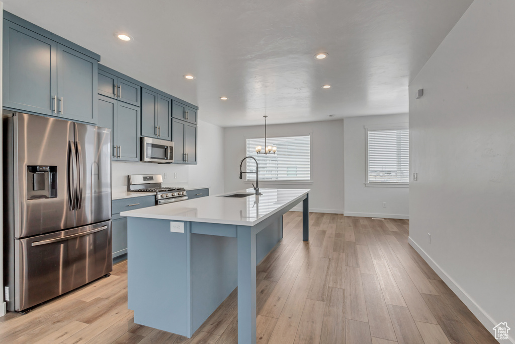 Kitchen with decorative light fixtures, light hardwood / wood-style flooring, an island with sink, appliances with stainless steel finishes, and sink