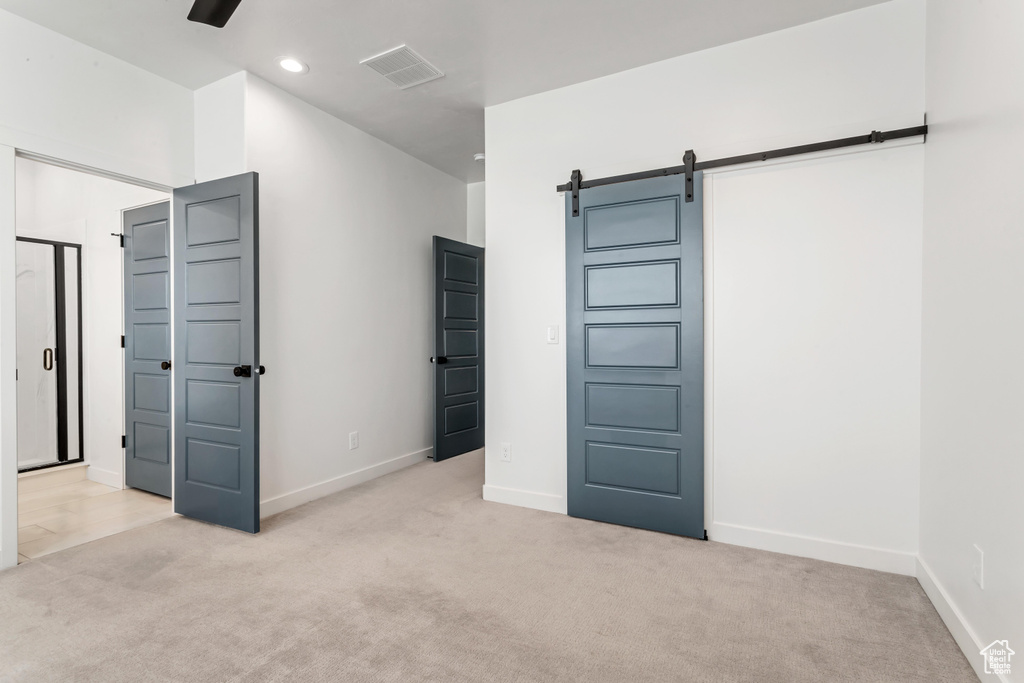 Unfurnished bedroom featuring light carpet, a barn door, and ceiling fan