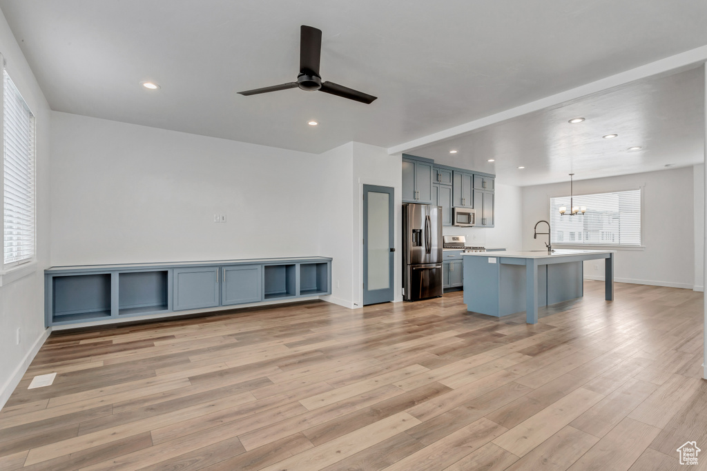 Kitchen with light hardwood / wood-style flooring, decorative light fixtures, a kitchen bar, a kitchen island with sink, and appliances with stainless steel finishes