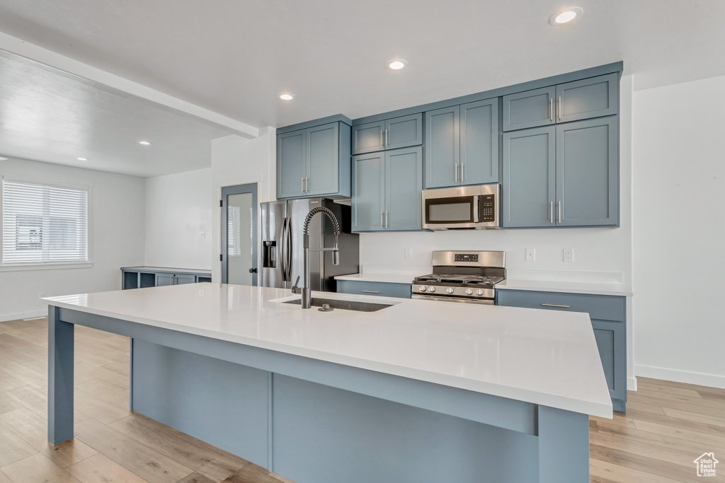 Kitchen with stainless steel appliances, sink, an island with sink, and light wood-type flooring