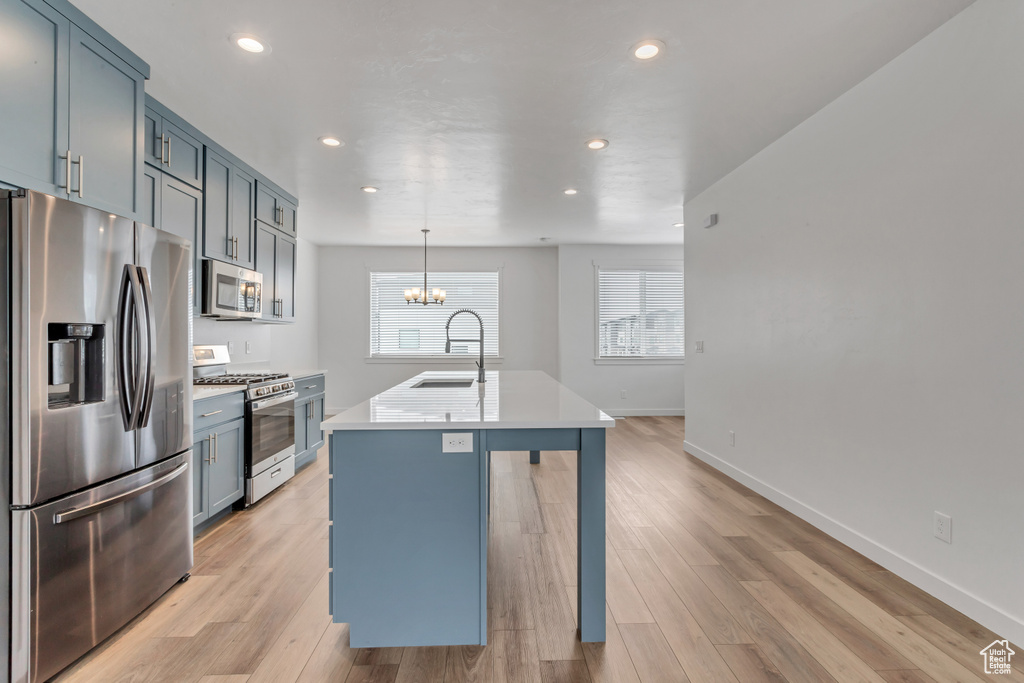 Kitchen featuring light hardwood / wood-style flooring, an island with sink, stainless steel appliances, hanging light fixtures, and sink