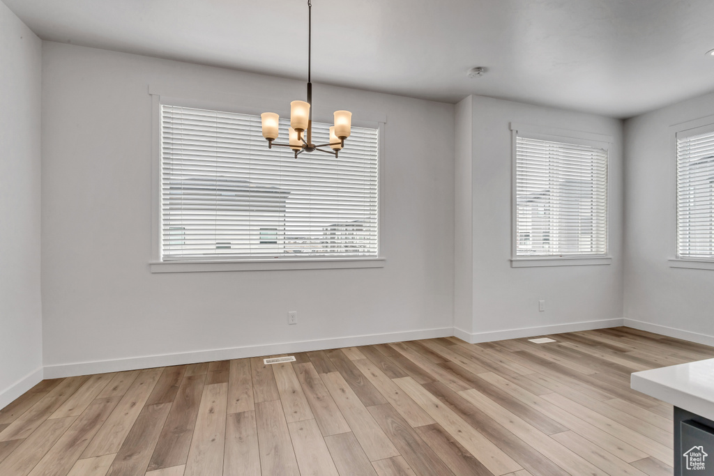 Unfurnished room featuring an inviting chandelier and light hardwood / wood-style flooring