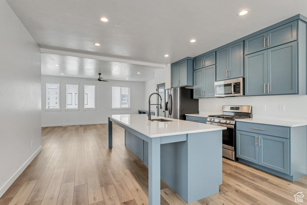 Kitchen with ceiling fan, stainless steel appliances, a center island with sink, light wood-type flooring, and blue cabinets