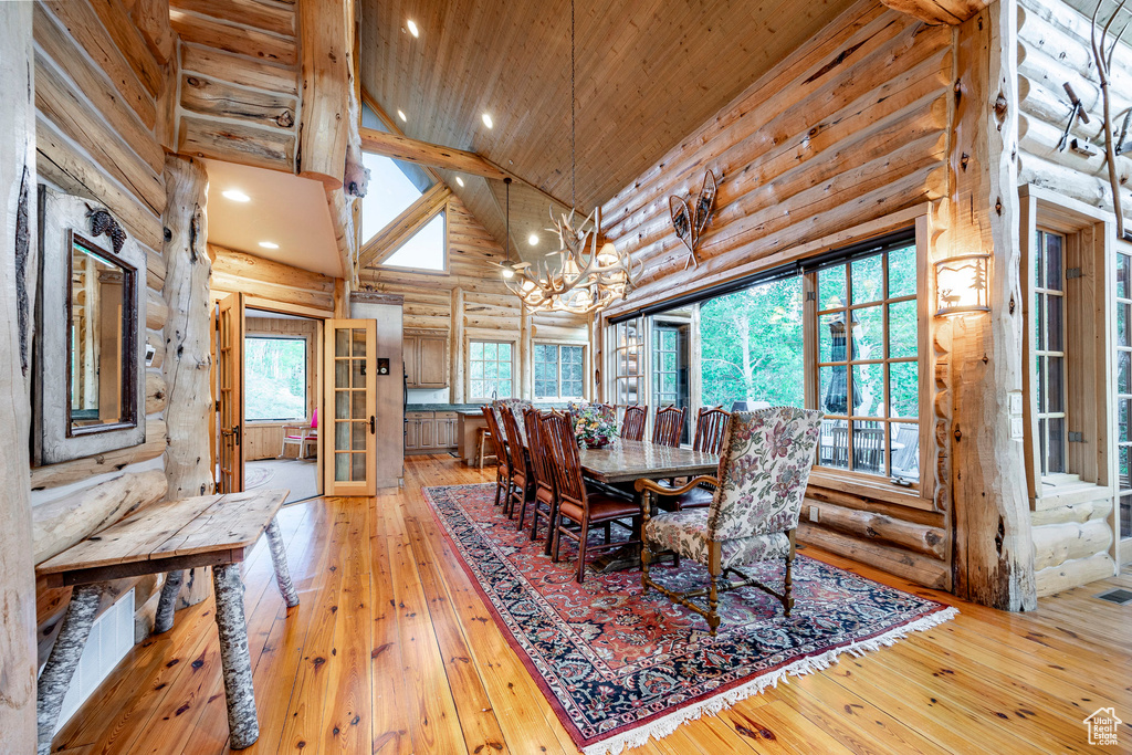 Dining area with light hardwood / wood-style flooring, wooden ceiling, a chandelier, high vaulted ceiling, and rustic walls