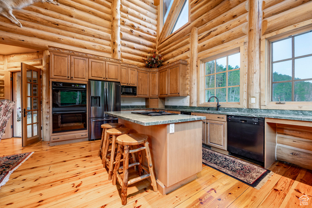 Kitchen featuring a center island, black appliances, light hardwood / wood-style floors, and log walls