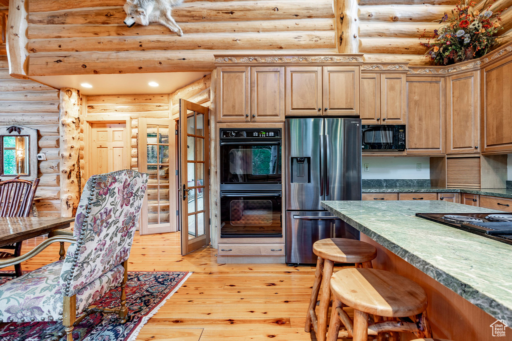 Kitchen featuring a kitchen bar, black appliances, log walls, and light wood-type flooring