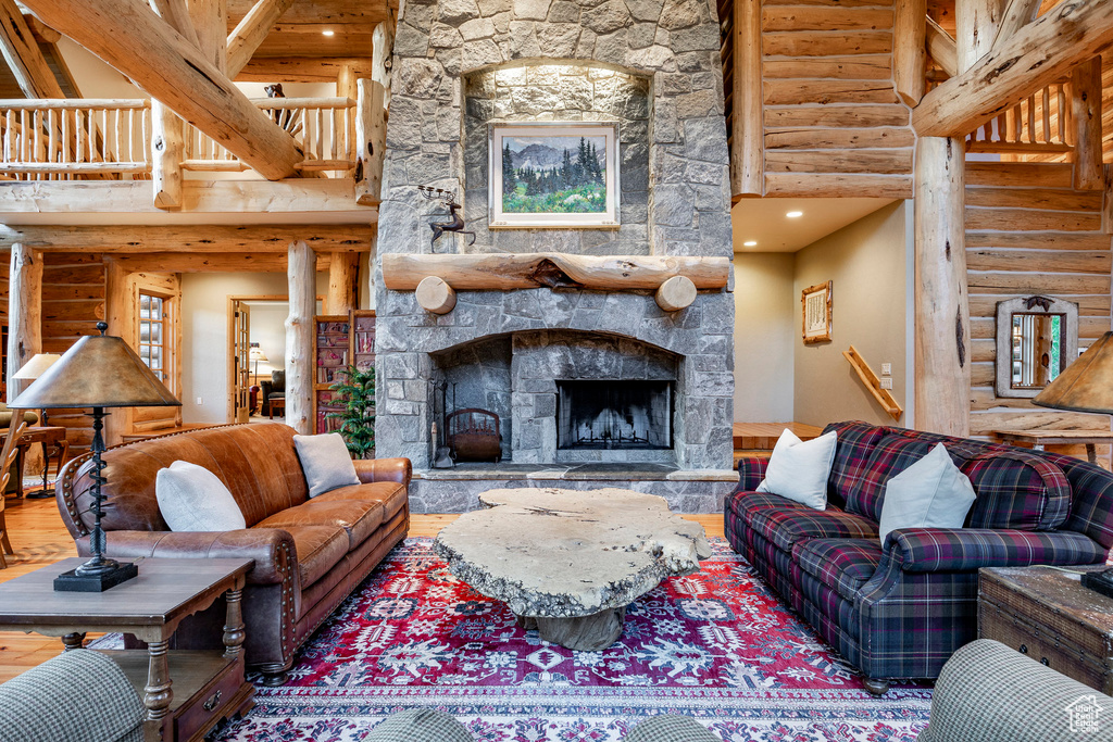 Living room featuring a stone fireplace, a towering ceiling, hardwood / wood-style flooring, and rustic walls