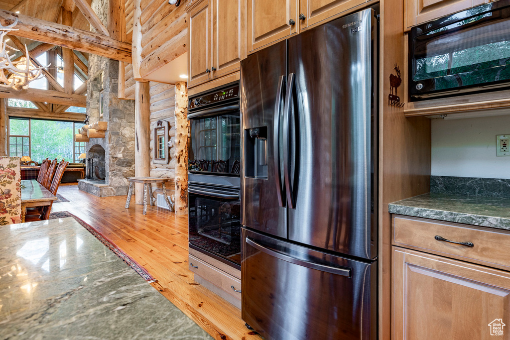 Kitchen featuring a stone fireplace, a towering ceiling, light hardwood / wood-style flooring, and black appliances