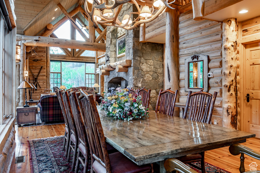 Dining room with beamed ceiling, wood-type flooring, an inviting chandelier, high vaulted ceiling, and log walls