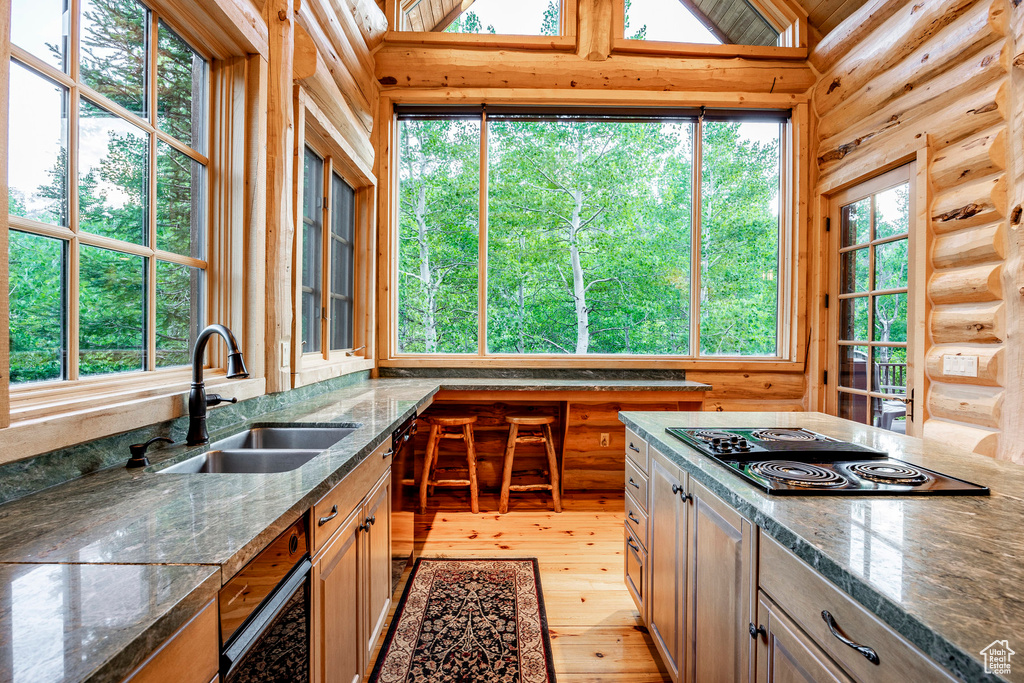 Kitchen featuring sink, black electric cooktop, light wood-type flooring, and rustic walls