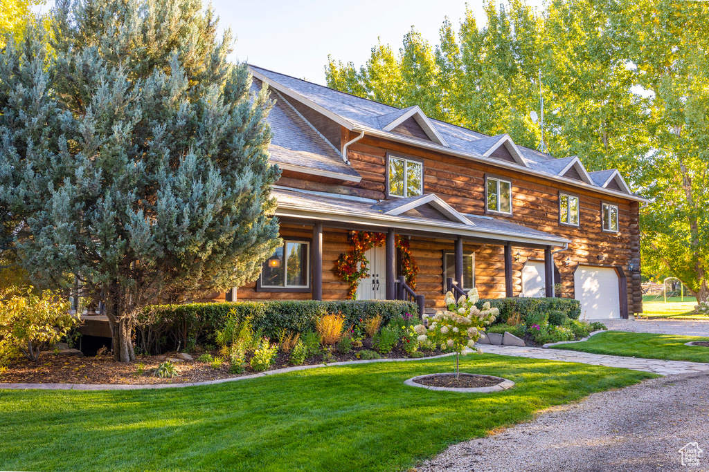View of front of house with an attached garage, a front yard, covered porch, log siding, and driveway