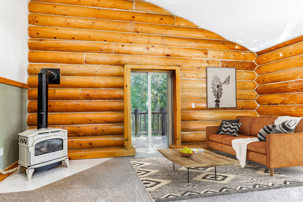 Living area with a wood stove, rustic walls, baseboards, and vaulted ceiling