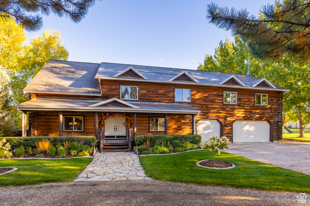 Log home featuring a front yard, driveway, a garage, covered porch, and log exterior