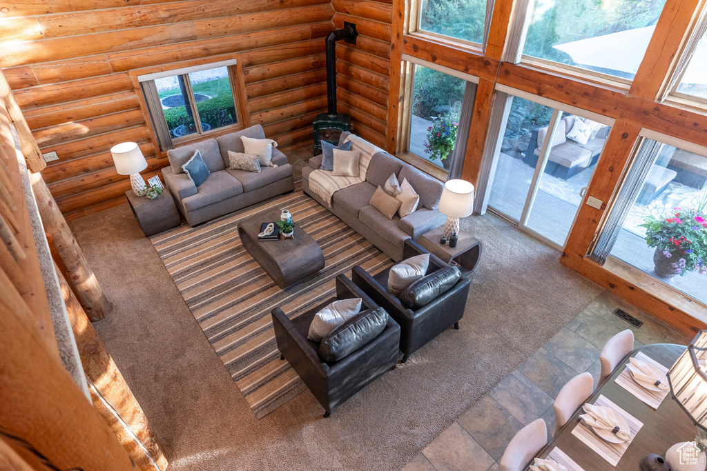 Living room with carpet flooring, log walls, a wood stove, and a towering ceiling