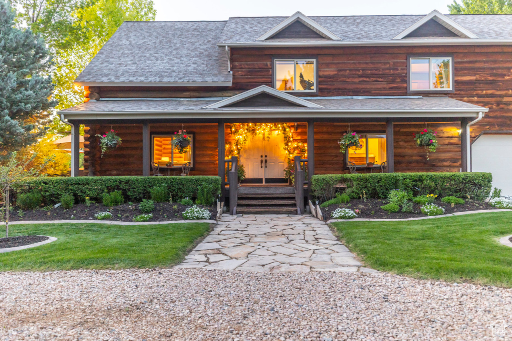 View of front facade featuring covered porch, roof with shingles, and a front yard