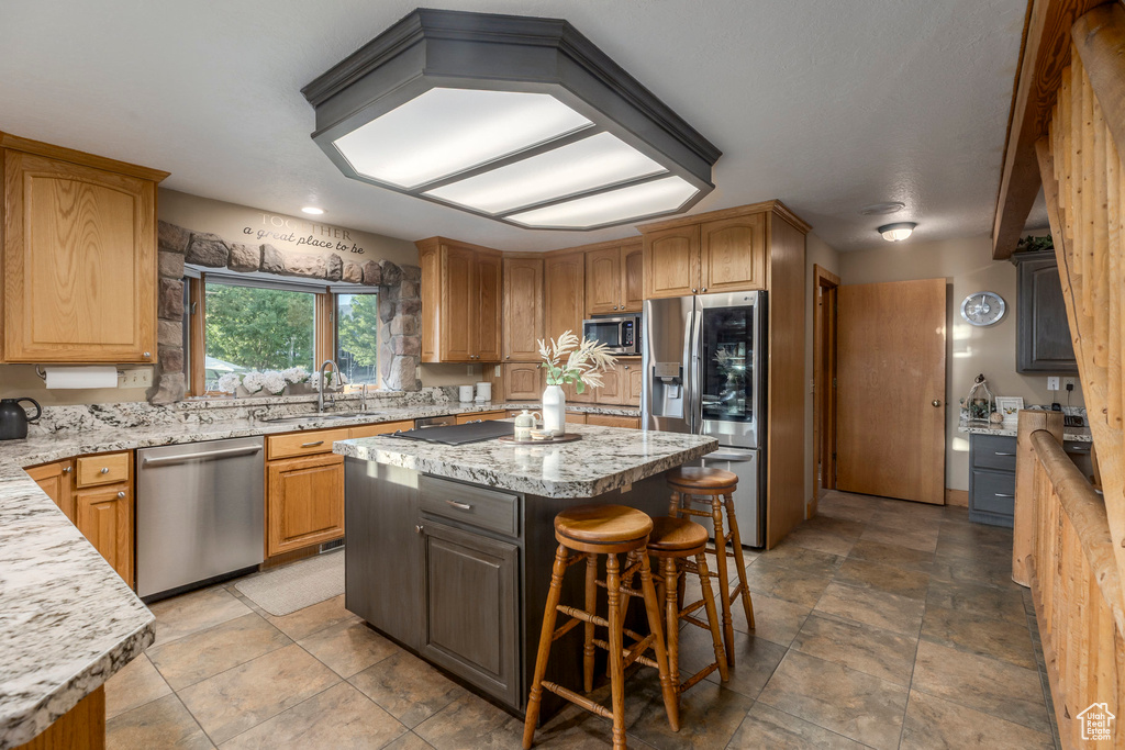 Kitchen featuring stainless steel appliances, a sink, a kitchen island, a breakfast bar area, and light stone counters